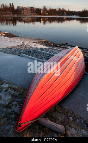 Red fiberglass rowboat / skiff / dinghy , upturned for Winter storage , is covered with frost , Finland Stock Photo