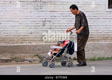 A Chinese man pushing a pram with a baby in the street of HoHot, Inner Mongolia, northern China Stock Photo