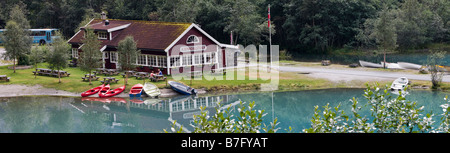 Panoramic travel photograph of tiny tourist at picnic table, scenic Cafe Kjenndalstova, water, boats, en-route to Jostedalsbreen National Park, Norway Stock Photo