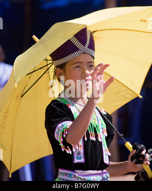 A young Hmong girl in traditional dress prepares to catch a ball at a Hmong New Year ceremony, shaded by a yellow umbrella. Stock Photo