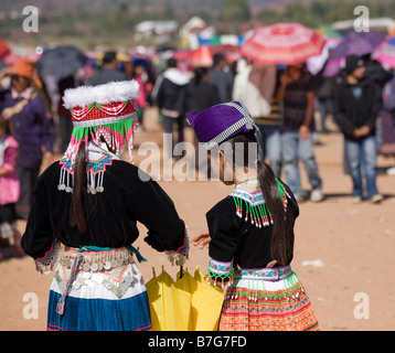 A view from behind of two Hmong girls in traditional costume walking through the crowd at a Hmong New Year ceremony. Stock Photo