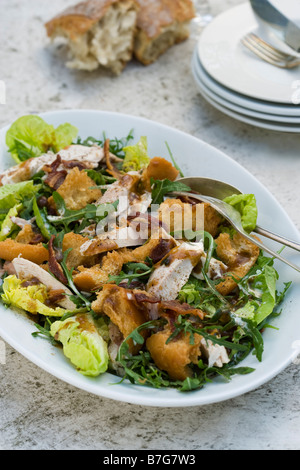 Chicken Caesar Salad on a table top with plates and bread in the background Stock Photo