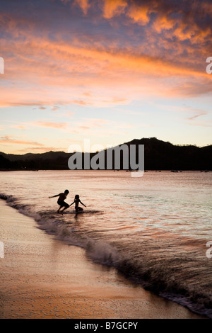 Silhouette of two children playing in the surf at sunset on the beach of Playas del Coco, Guanacaste, Costa Rica.