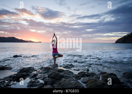 Young woman practicing yoga at sunset in front of ocean surf at Playas del Coco, Guanacaste, Costa Rica.