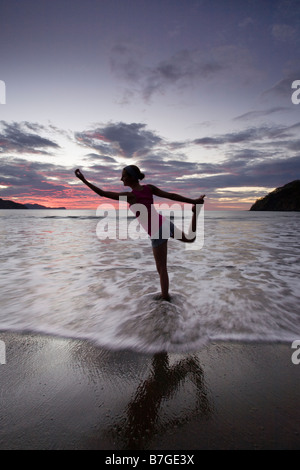 Young woman doing yoga in the surf at the beach during sunset in Playas del Coco, Guanacaste, Costa Rica.