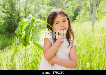 Young Asian girl holding plant stem in field