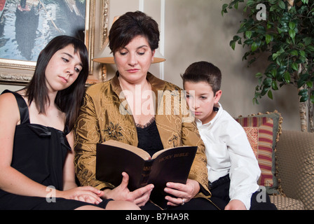 A woman teaches her two children by reading to them from the Bible Stock Photo