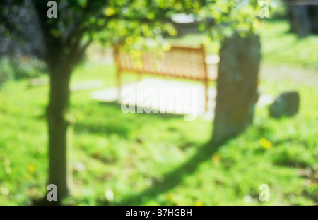 Impressionistic view of sunlit churchyard with new wooden bench grass gravestones and Flowering cherry tree in early autumn Stock Photo