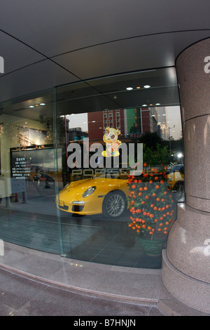 Porsche Dealership Window in China with Chinese New Year Decorations and orange tree in show room next to Yellow Carrera Stock Photo