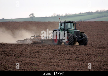 Farmer using harrow on ploughed field in dry dusty drought like conditions.