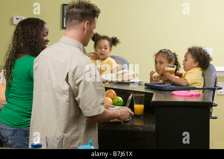 Caucasian dad and AA mom preparing a meal for their Mulatto children, boy 1.5 years, girl 3 and 6 years. Stock Photo