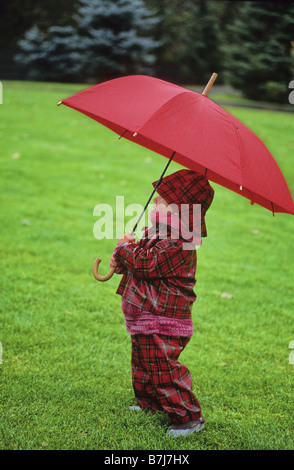 Boy, 2, in red tartan rainsuit, holds red umbrella, Whistler, BC Stock Photo