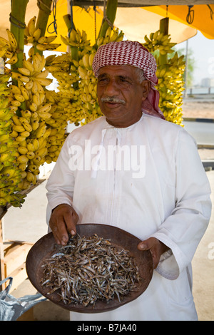 Local market fruit seller (MR) wearing turban selling bananas & dried fish, seafood, prepared snack in Ras Al Khaimah Old town Market, Dubai, UAE Stock Photo