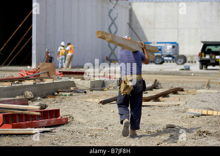 Construction worker carrying wood beams across a construction site; Canada, Ontario, Hamilton Stock Photo