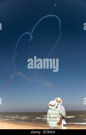 Elderly couple hold one another with Red Arrows heart in sky behind them Stock Photo