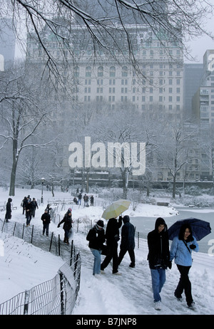 New York City snow scene fog winter weather. Groups of people walking through Central Park during a snowstorm. View of the Plaza Hotel Stock Photo