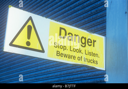 Detail of warehouse with pale grey slatted wall and dark gray roller door with sign Danger Stop Look Listen Beware of trucks Stock Photo