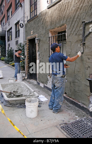 Two workers repair the exterior wall of a combination commercial and apartment building in an urban city Stock Photo