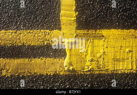 Detail from above of bright double yellow lines on road edge with additional yellow paint thickly applied to create box