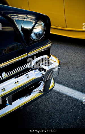 A bright yellow hot rod and black custom car parked in an asphalt parking lot. Stock Photo