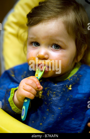 A baby girl spoon feeds herself a strawberry. Stock Photo