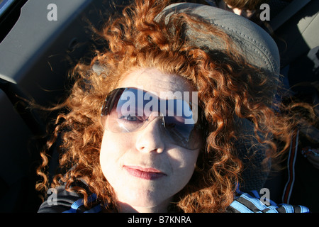 close up of woman laying down in sunshine, convertible car, wearing sunglasses, outdoors, black leather interior Stock Photo