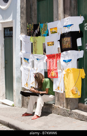 Young woman sitting on step below colourful hand-painted T-shirts for sale as souvenirs for tourists in Brazil Stock Photo