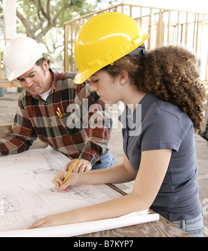 A female engineering student on a construction site marking blueprints as her instructor watches Stock Photo