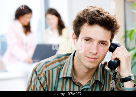 Young office workers working at office businessman in front calling on phone looking at camera smiling Stock Photo