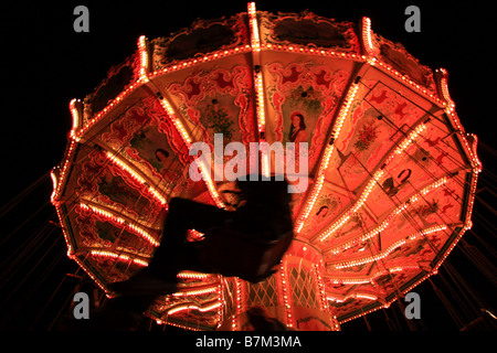 Silhouetted rider on traditional chained seat carousel ride at Winter Wonderland, Hyde Park, London Stock Photo