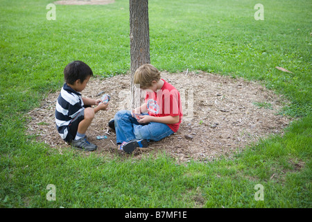 two school age boys playing a trading card game outdoors in public park, japanese boy and american boy Stock Photo