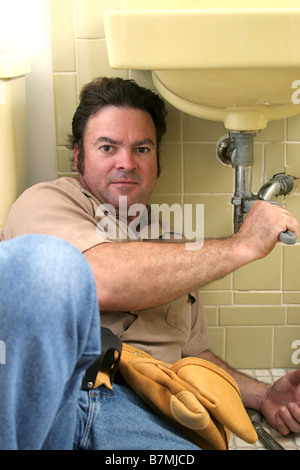 A plumber working on a sink in a bathroom Stock Photo