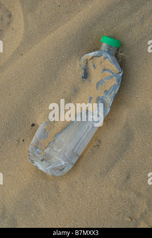 An empty smashed plastic water bottle in a sandy beach