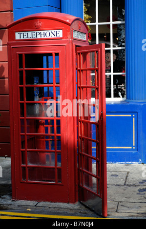 Traditional English red phone box with an open door outside in front of a blue wall building Stock Photo
