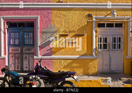 Two bikes on the street in front of a brightly colored building of pink and yellow