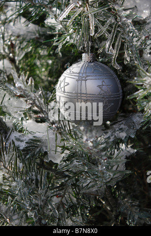 Frosty Christmas silver ball hanging on a frozen branch of a tree outside in Winter nobody closeup close up from front vertical hi-res Stock Photo