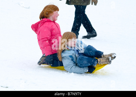 Two Girls Children riding on a sled sledge sledging in the Snow Stock Photo