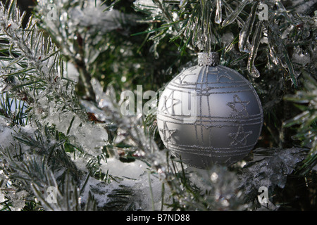 Frosty Christmas silver ball hanging on a frozen branch of a tree outside in Winter nature nobody closeup close up  from front horizontal hi-res Stock Photo