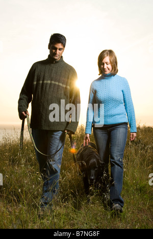couple walking dog outdoors at sunset in california on hill Stock Photo