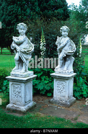 Twin stone cherubs on plinths with white foxgloves in a country garden Stock Photo