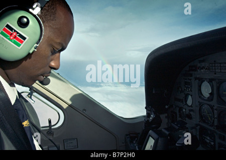 A pilot of a small chartered aeroplane flying over Northern Kenya. A rainbow arches in the background sky. Northern Kenya. Stock Photo