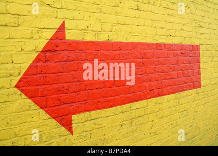 A large red arrow on a painted yellow brick wall Stock Photo