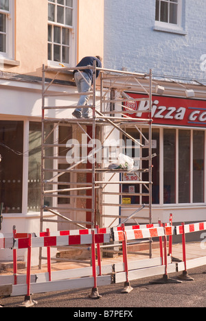 Man working on a building from a tower scaffold with safety barriers Stock Photo