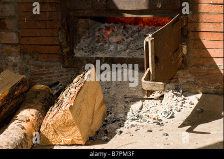 Chopped wood in front of the oven and fire burning in the oven. Stock Photo