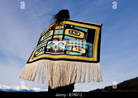 Native Alaskan wearing a Chilkat Blanket while looking upward at a soaring Bald Eagle in Alaska. Composite Stock Photo