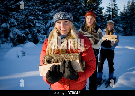 Three young women on snowshoes hauling chopped wood near Homer, Alaska during winter. Stock Photo