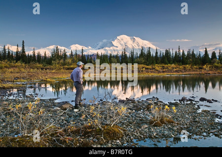 Man stands next to a small lake with Mt. McKinley and the Alaska Range in the background in Denali National Park, Alaska Stock Photo