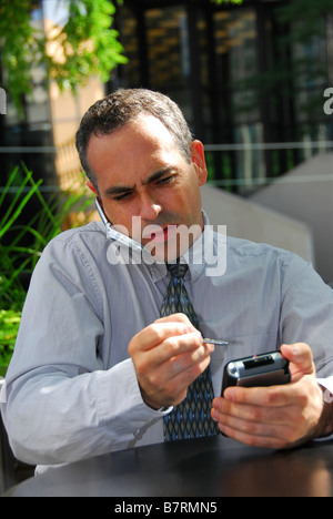Busy businessman talking on cell phone and working on his palm pilot Stock Photo