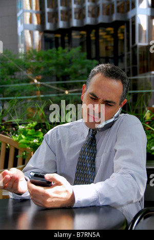 Portrait of a busy businessman in the city using pda and cell phone Stock Photo