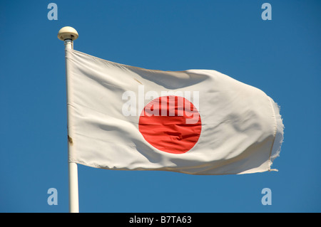 Japanese flag flying on a white flagpole seen against a blue sky. Stock Photo